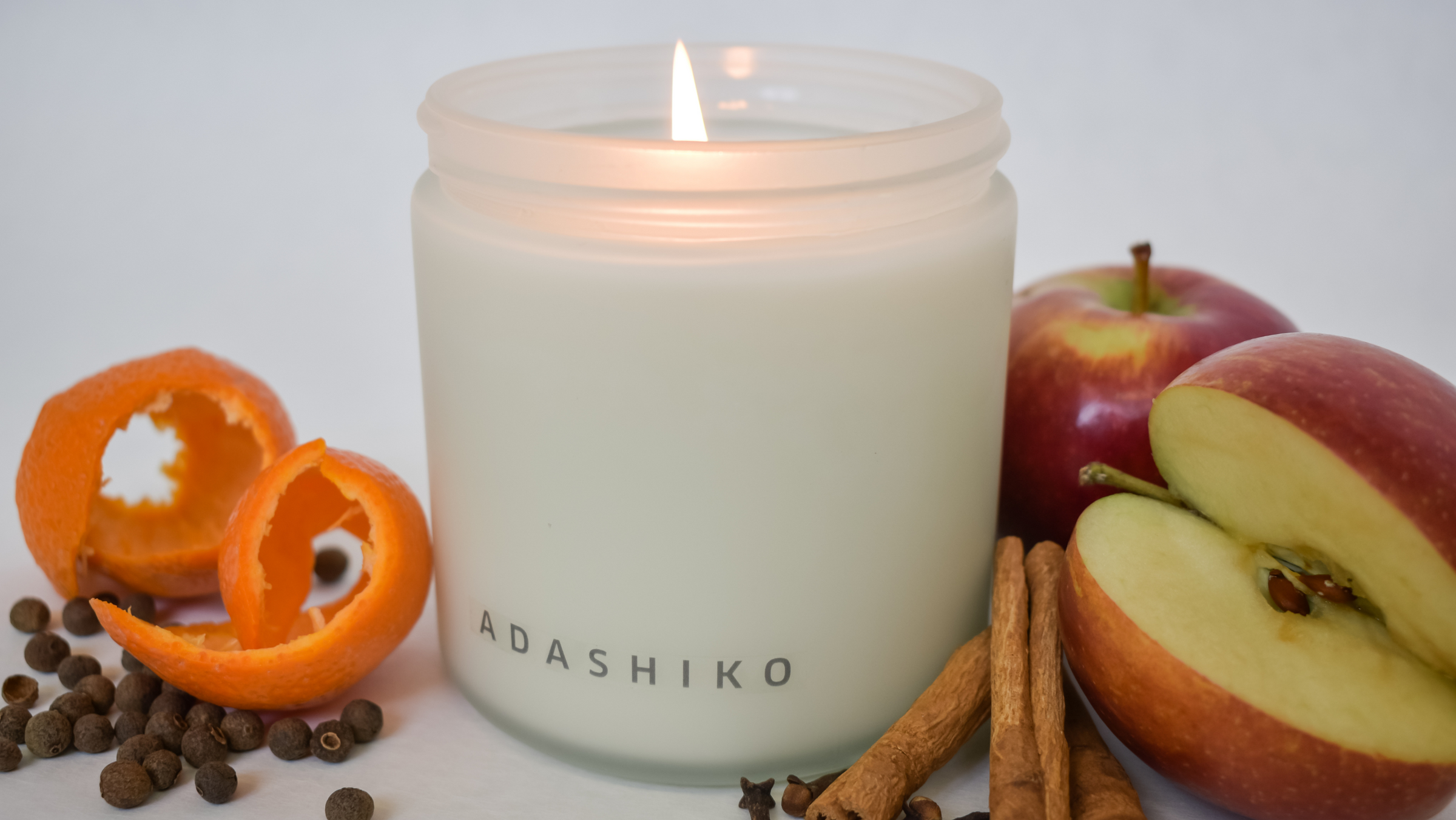 Joy Christmas Candle lit surrounded by its scent ingredients | Adashiko Collagen | 100% Natural Skincare