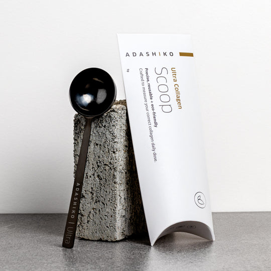 Adashiko Ultra Collagen scoop and packaging on a gray surface with a white background | Adashiko Collagen | 100% Natural Skincare