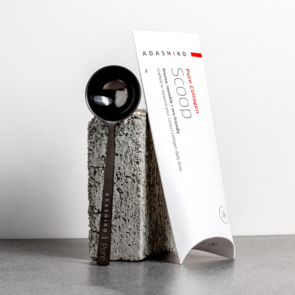 Adashiko Pure Collagen scoop and packaging on a gray surface with a white background | Adashiko Collagen | 100% Natural Skincare