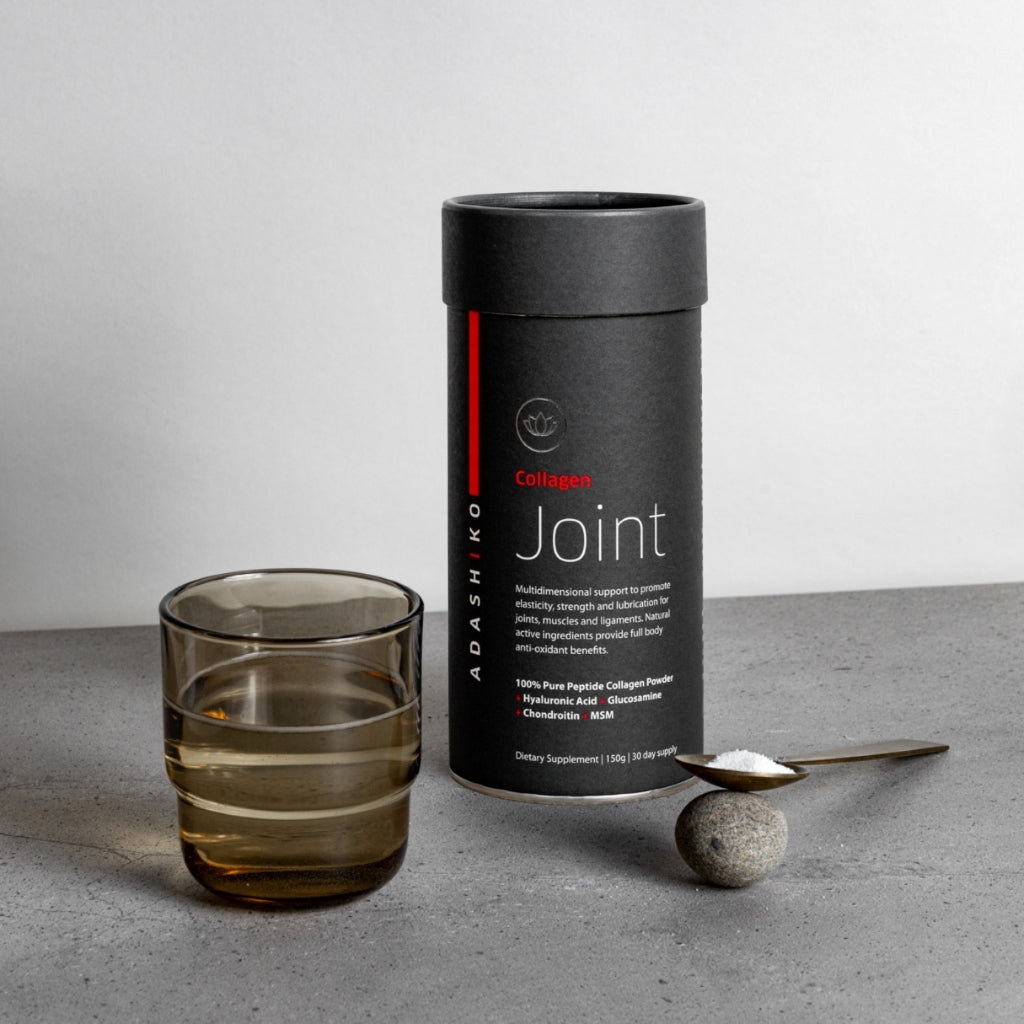 Tub of Joint Collagen Powder next to a glass of water and a spoon with powder against a grey background | Adashiko Collagen | 100% Natural Skincare