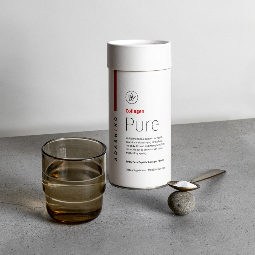 Tub of Pure Collagen Powder next to a glass of water and a spoon with powder against a grey background | Adashiko Collagen | 100% Natural Skincare