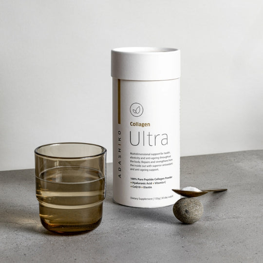 Tub of Ultra Collagen Powder next to a glass of water and a spoon with powder against a grey background | Adashiko Collagen | 100% Natural Skincare