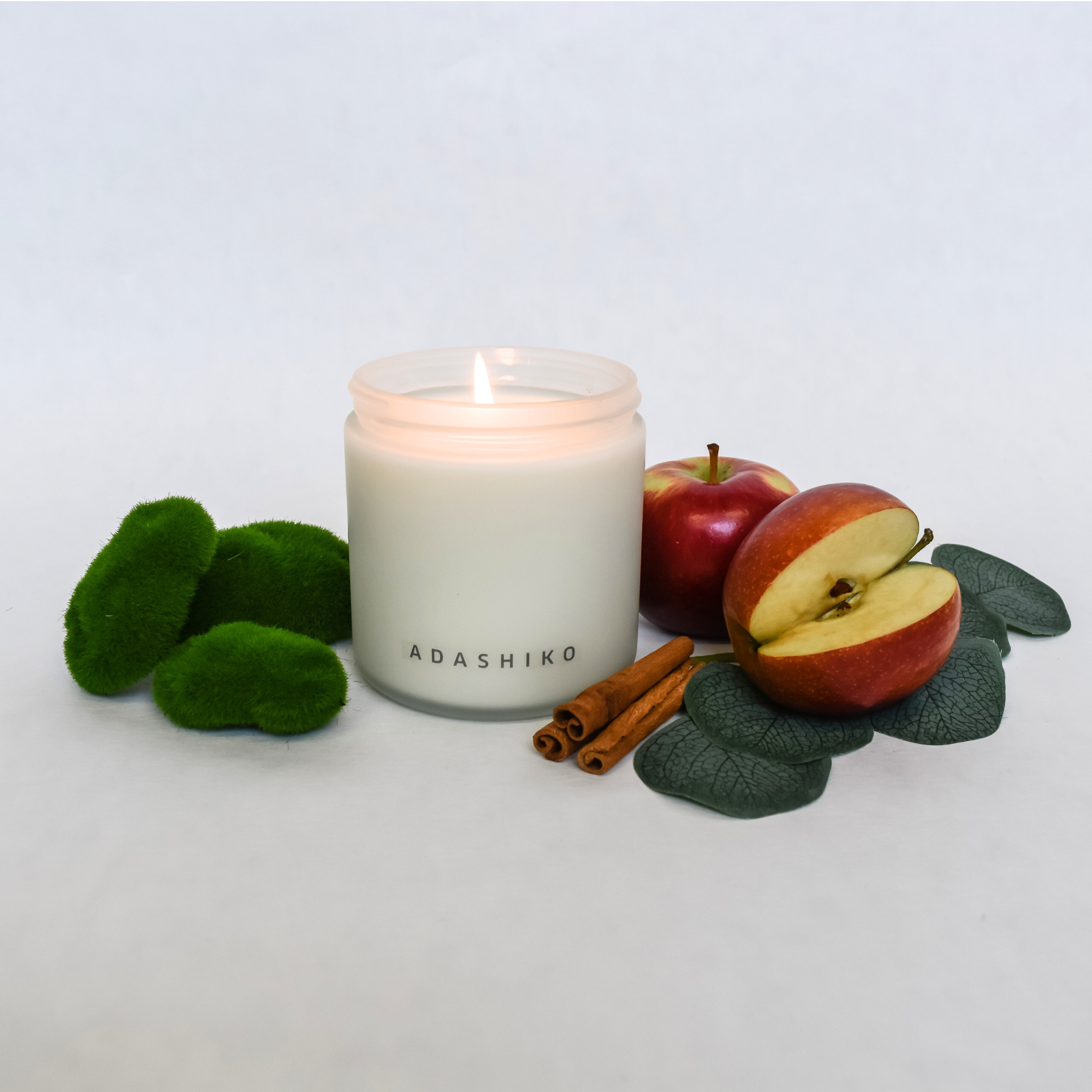 Woodlands Christmas Candle lit surrounded by its scent ingredients | Adashiko Collagen | 100% Natural Skincare
